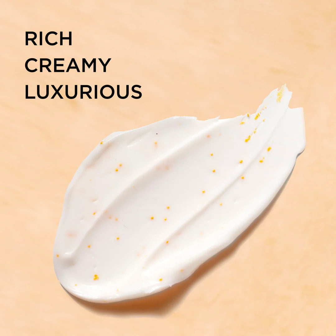 A thick, creamy white cosmetic smear with tiny golden-yellow specks on a warm beige background, with the text 'RICH CREAMY LUXURIOUS' in black at the top left.