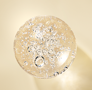 A top-down close-up of a clear, bubble-filled circular gel or resin sample on a warm beige background.