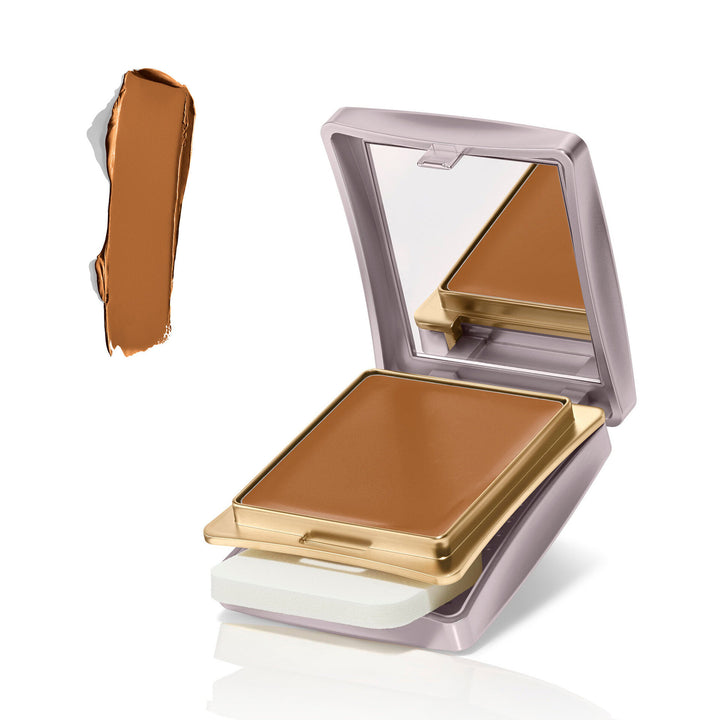 An open square pressed powder compact with a mirror in the lid, shown on a white background with a vertical smear of the brown powder beside it. The compact has a pale lavender exterior with gold trim and a white powder pan visible underneath.