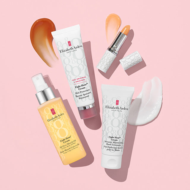 Four Elizabeth Arden skincare products arranged on a soft pink background: a yellow bottle of Light-Flowing Serum, a white tube of Eight Hour Cream, a white tube of Skin Prompts Q-Tip, and a lipstick with a sponge tip, plus cream smears and a white eye mask sheet.