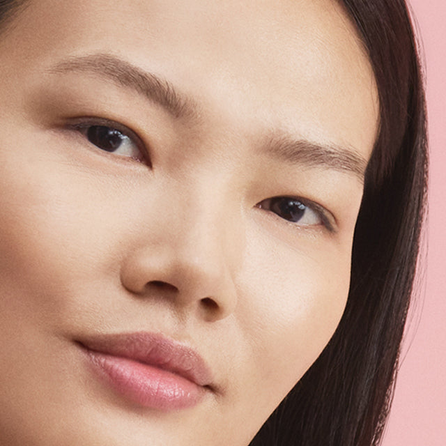 Close-up of a person's face with a neutral expression on a pink background